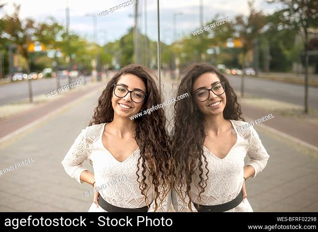 Smiling young woman with long hair standing on sidewalk by modern building in city