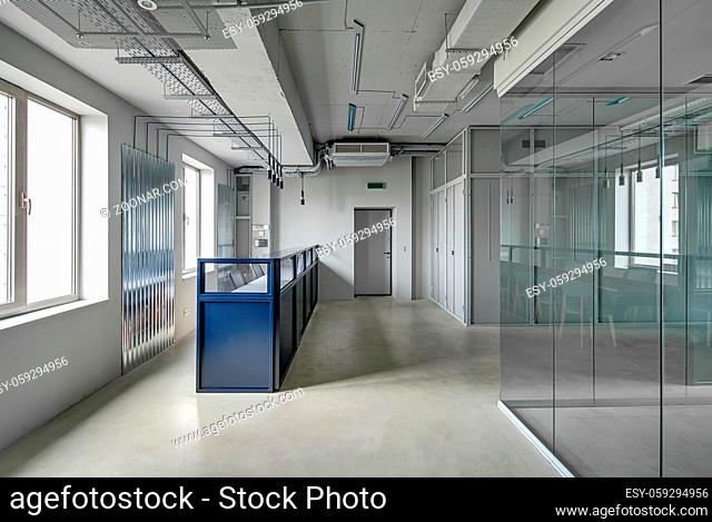 Blue metal reception rack with armchairs in a loft style office with gray walls. There is an entrance door and work zones with glass and mesh partitions