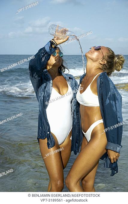 Two women playing with water bottles at beach, Chersonissos, Crete, Greece