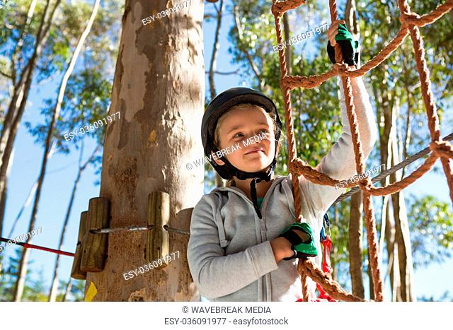 Little girl wearing helmet getting ready to climb on rope fence