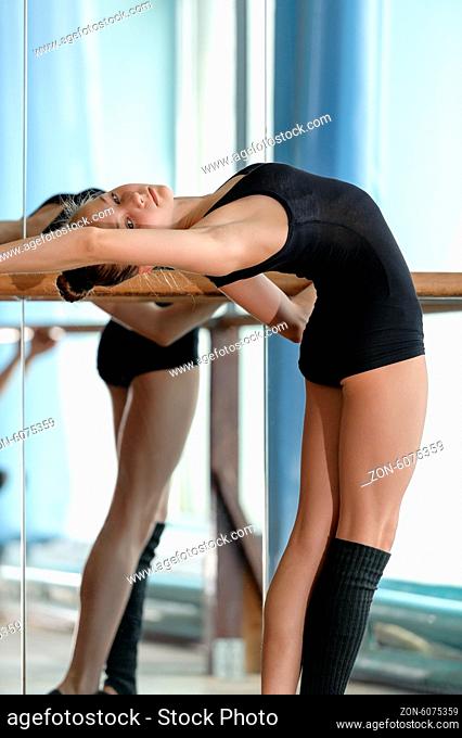 Young graceful ballet dancer stretching out at the barre in the studio