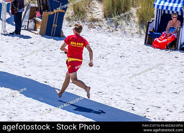 15 July 2021, Mecklenburg-Western Pomerania, Prerow: Lifeguard Pascal Greinert of the DLRG water rescue team runs across the beach next to the pier during an...