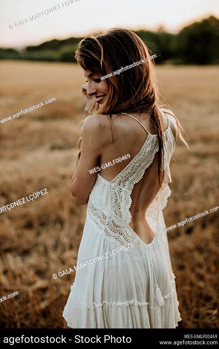 Woman wearing white dress looking over shoulder while standing in wheat field