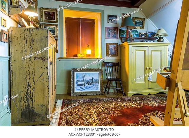 Artist's upstairs studio with closed wooden shutters on window, easel and paintings on the walls plus ocre and yellow antique wooden armoires inside an old...