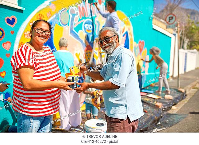 Portrait happy community volunteers painting mural on sunny urban wall