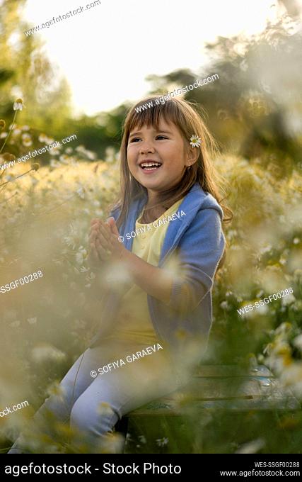 Happy girl in casual clothing sitting amidst plants in meadow