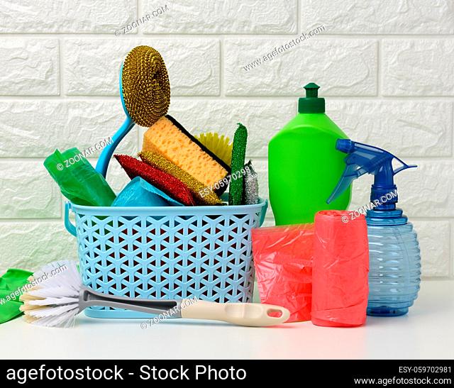 plastic basket with brushes, disinfectant in a bottle, rubber gloves on the background of a white brick wall. House cleaning items set