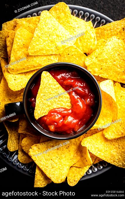 Tortilla chips and red tomato salsa dip. Mexican nacho chips on black table. Top view