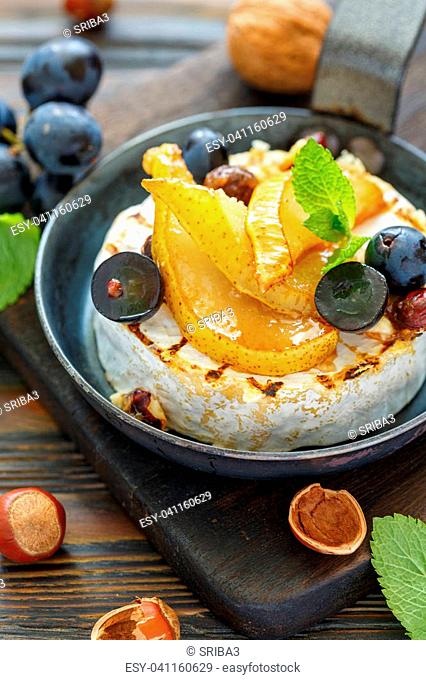 Grilled camembert with pears and black grapes in a cast iron pan on a wooden stand, selective focus