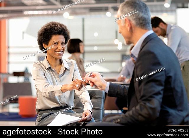 Smiling businesswoman taking pen from colleague in office