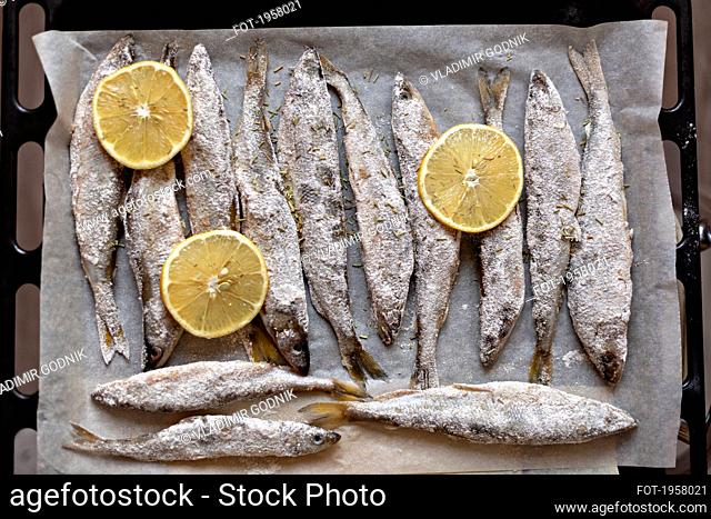 Fresh salted whole fish and lemon slices on parchment paper