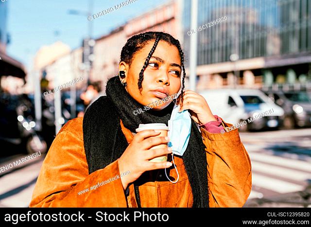 Italy, Young woman with face mask holding disposable cup outdoors