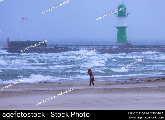 16 November 2023, Mecklenburg-Western Pomerania, Rostock: A woman walks across the beach on the Baltic Sea coast in Warnemünde in the storm and rain