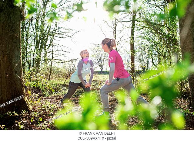 Women face to face in forest hands on knee lunging