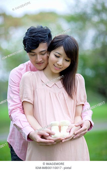 Young man and pregnant woman holding a pair of baby shoes with smile together