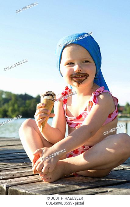 Portrait of female toddler on pier eating chocolate ice cream cone, Lake Seeoner See, Bavaria, Germany