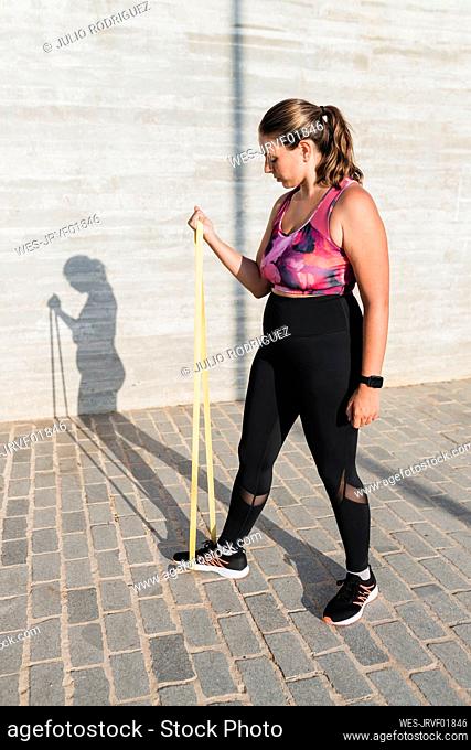 Young female athlete with resistance band practicing during sunny day