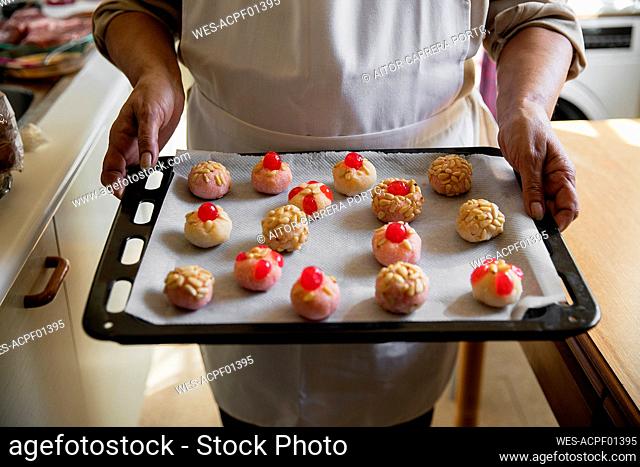 Woman with apron holding panellets in baking sheet at kitchen