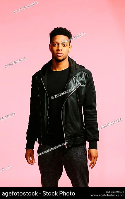 Half body portrait of a serious urban African American man in black isolated on pink background
