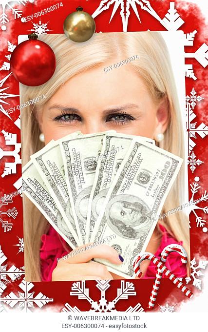 Blonde hiding her face with dollars banknotes against christmas themed page