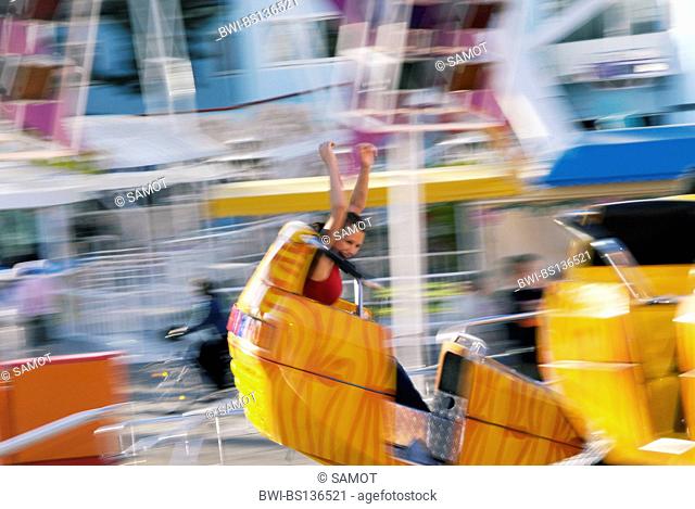 young woman in a carousel at the amusement park Wiener Prater, raising her arms in high spirits, Austria, Vienna