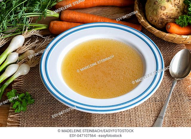 Chicken bone broth in a plate, with vegetables in the background