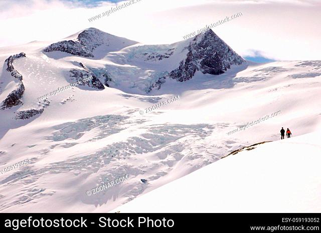 two backcountry skiers stand on a high alpine glacier in the Austrian Alps in winter under a blue sky
