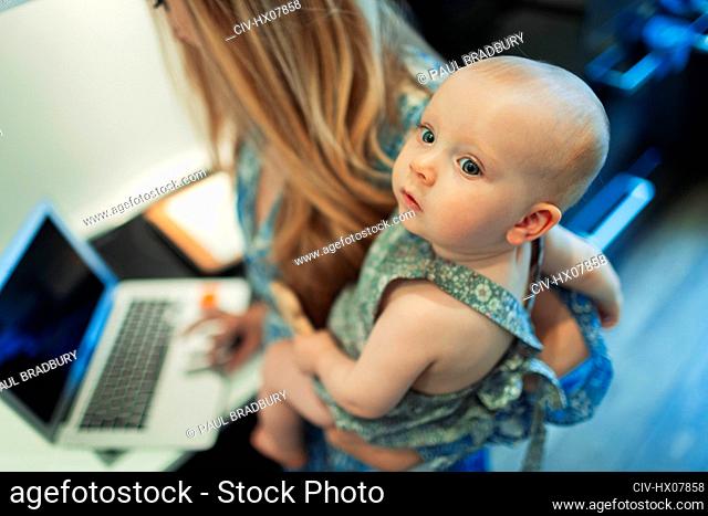 Mother working at laptop and holding cute baby daughter