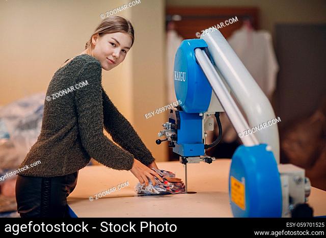 Young beautiful seamstress cutter clothing designer cuts fabric on the machine