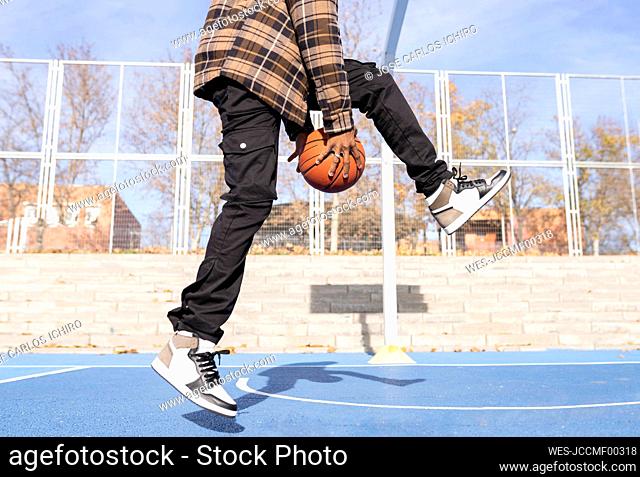 Young man playing basket ball in sports court on sunny day