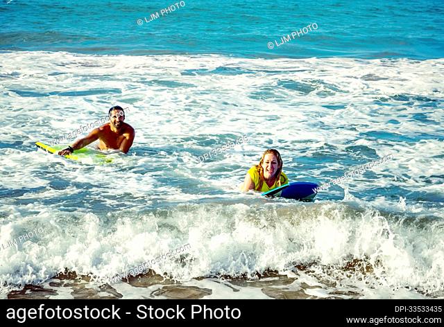 Happy married couple playing in the waves with bodyboards at D. T. Fleming Beach; Kapalua, Maui, Hawaii, United States of America