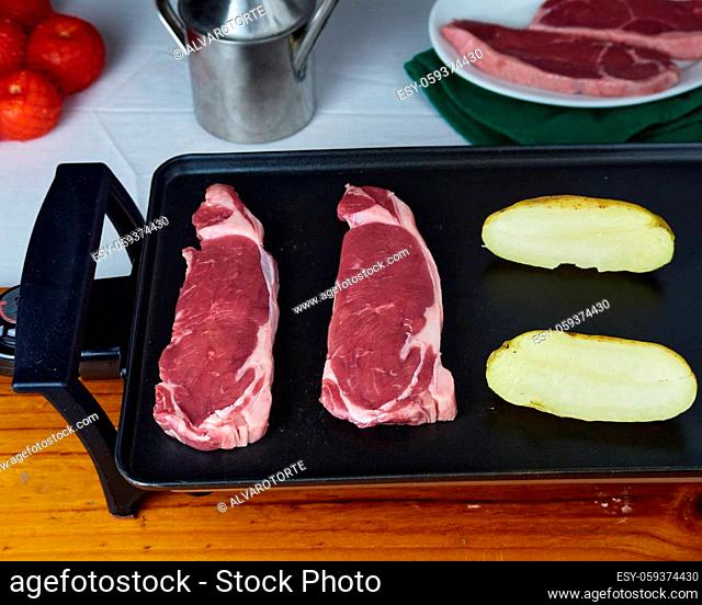 Raw Beefsteak with raw caliu potatoes on a electric griddle