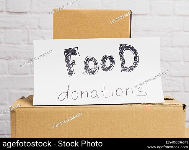 stack of cardboard boxes and white sheet of paper with inscription food donation on white brick wall background