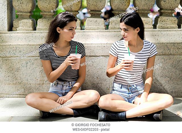 Two twin sisters sitting outdoors having a takeaway drink
