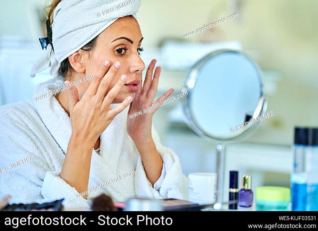 Woman applying cream on her face in front of mirror home