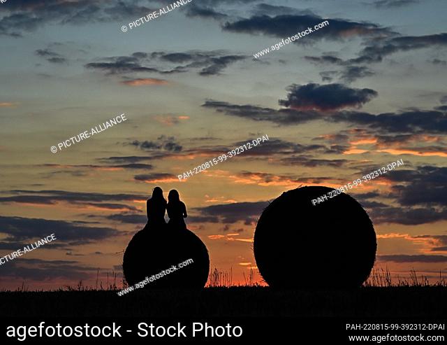 08 August 2022, Brandenburg, Jacobsdorf: Two girlfriends are sitting on a roll of straw in a field at sunset. Photo: Patrick Pleul/dpa