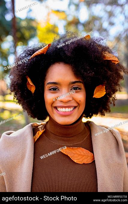 Curly hair woman with dry leaf on hair smiling while standing at park