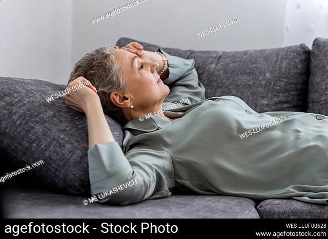 Mature woman lying on couch in living room with closed eyes