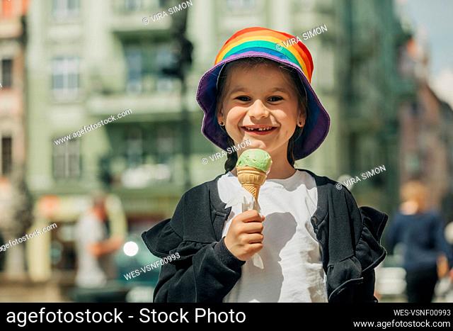 Smiling girl wearing colorful bucket hat holding ice cream