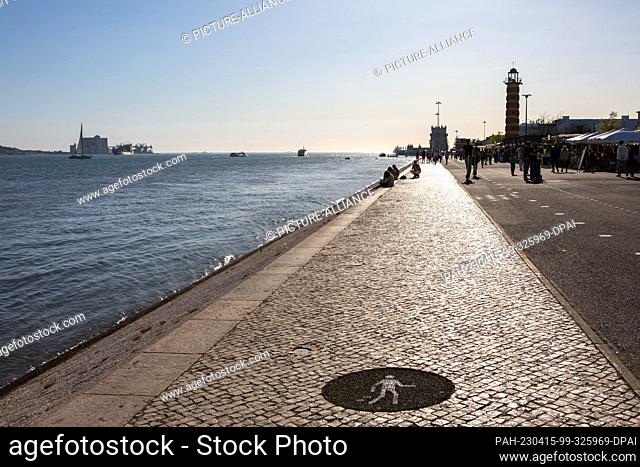 PRODUCTION - 06 April 2023, Portugal, Lissabon: Day trippers walk along the banks of the Tagus River in the early evening in the Belem district