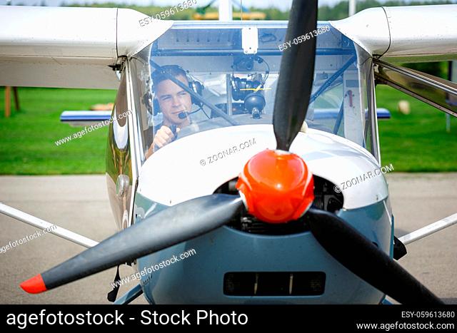 handsome teenage man sitting in small plane cockpit. young pilot with headset on. outdoor shot