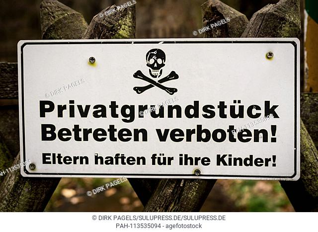 A white prohibition sign saying Private property. Enter prohibited! Parents are clinging to a hunter's fence somewhere in Berlin for their children with a skull...