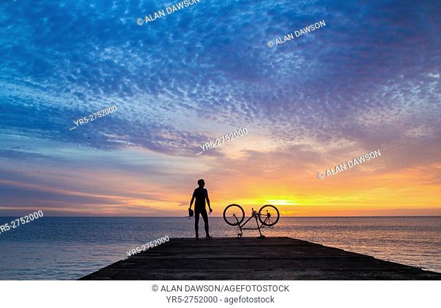 A mountain biker watches the sun rise over the North sea on a calm and tranquil morning at Seaton Carew, north east England, United Kingdom