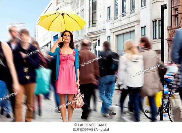 Mid adult woman in pink dress standing still with umbrella in crowded city