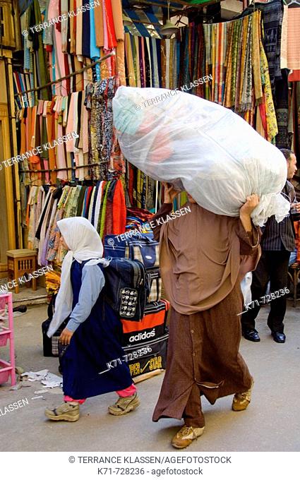 A muslim lady carrying a large bundle on her head through the streets of the Khan El Khalili market in Cairo, Egypt