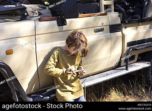 Eight year old boy leaning against a jeep, playing with a toy