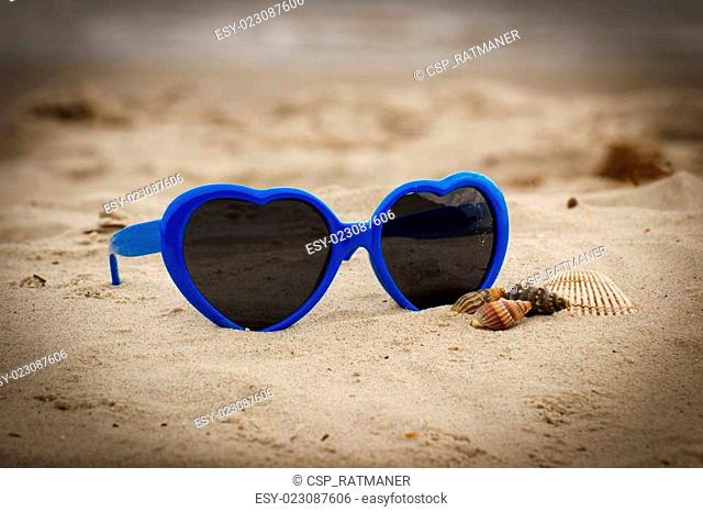 Blue sunglasses shaped heart with shells on the sand