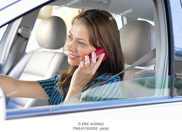 Beautiful young woman talking over mobile phone while driving a car