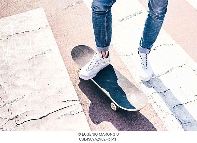 Legs and feet of young male skateboarder on pedestrian crossing