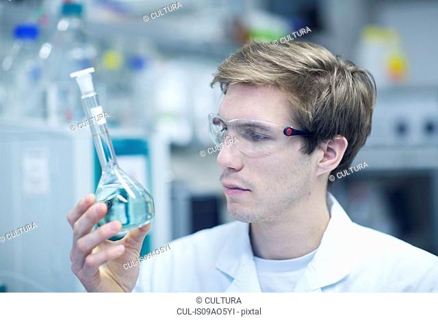 Male scientist holding up and looking at flask in lab